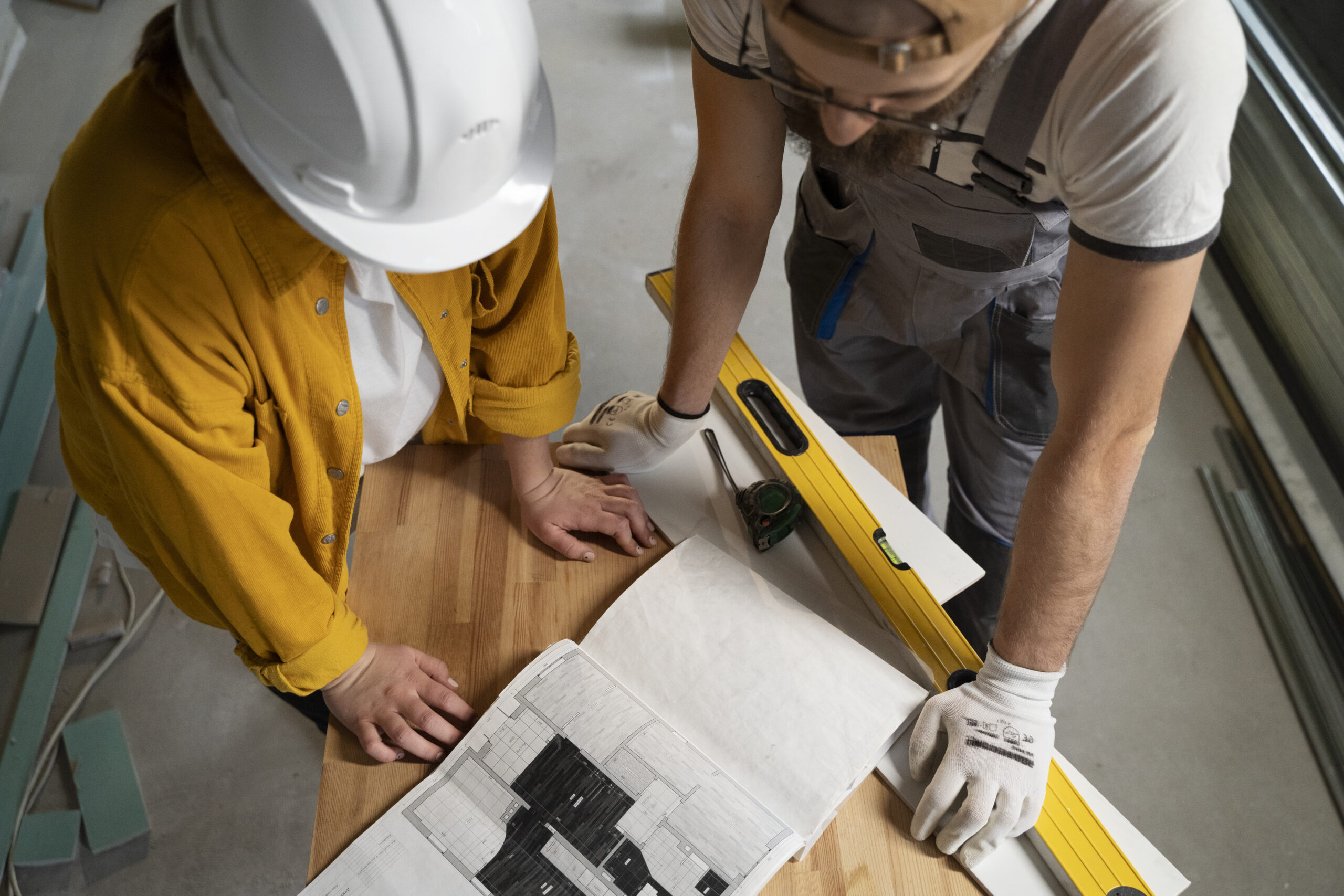 Two contractors reviewing apartment building renovation plans with blueprints and level tool on wooden floor