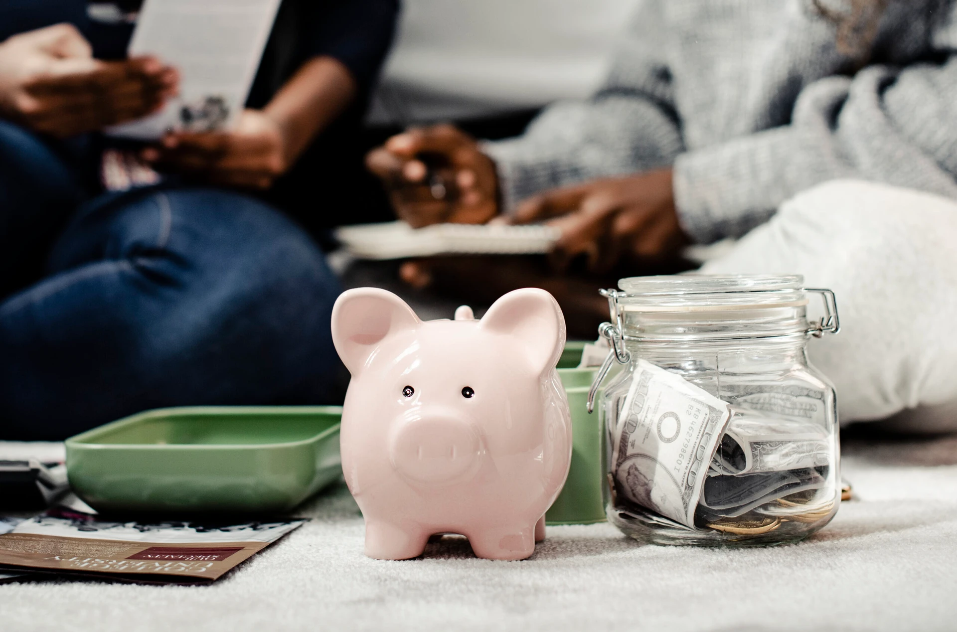 Piggy bank and jar of cash in foreground with people discussing financial strategies in the background—symbolizing collaborative planning and savings for multifamily investment and 1031 exchange reinvestment.