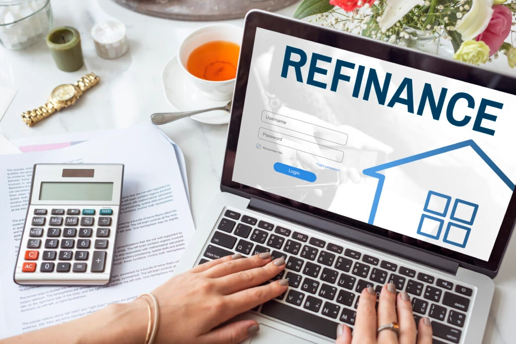 Person using a laptop with a refinance webpage open, surrounded by financial tools and documents—illustrating digital decision-making in multifamily investing.