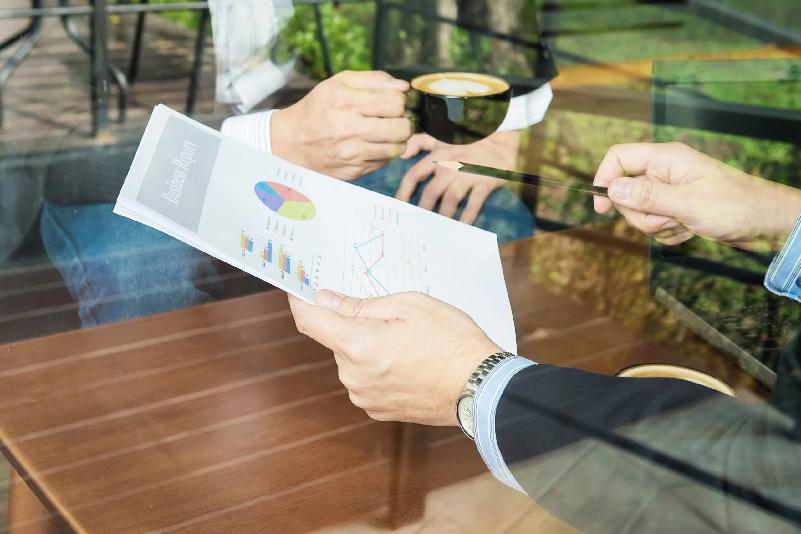 Two professionals reviewing a business report with charts and graphs while discussing debt service coverage ratio over coffee